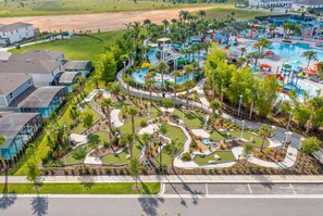 An aerial view of a resort with a large swimming pool, multiple water slides, and a well-maintained landscape with palm trees. - 5BR Themed Home w/ Game Room Near Disney (Davenport)
