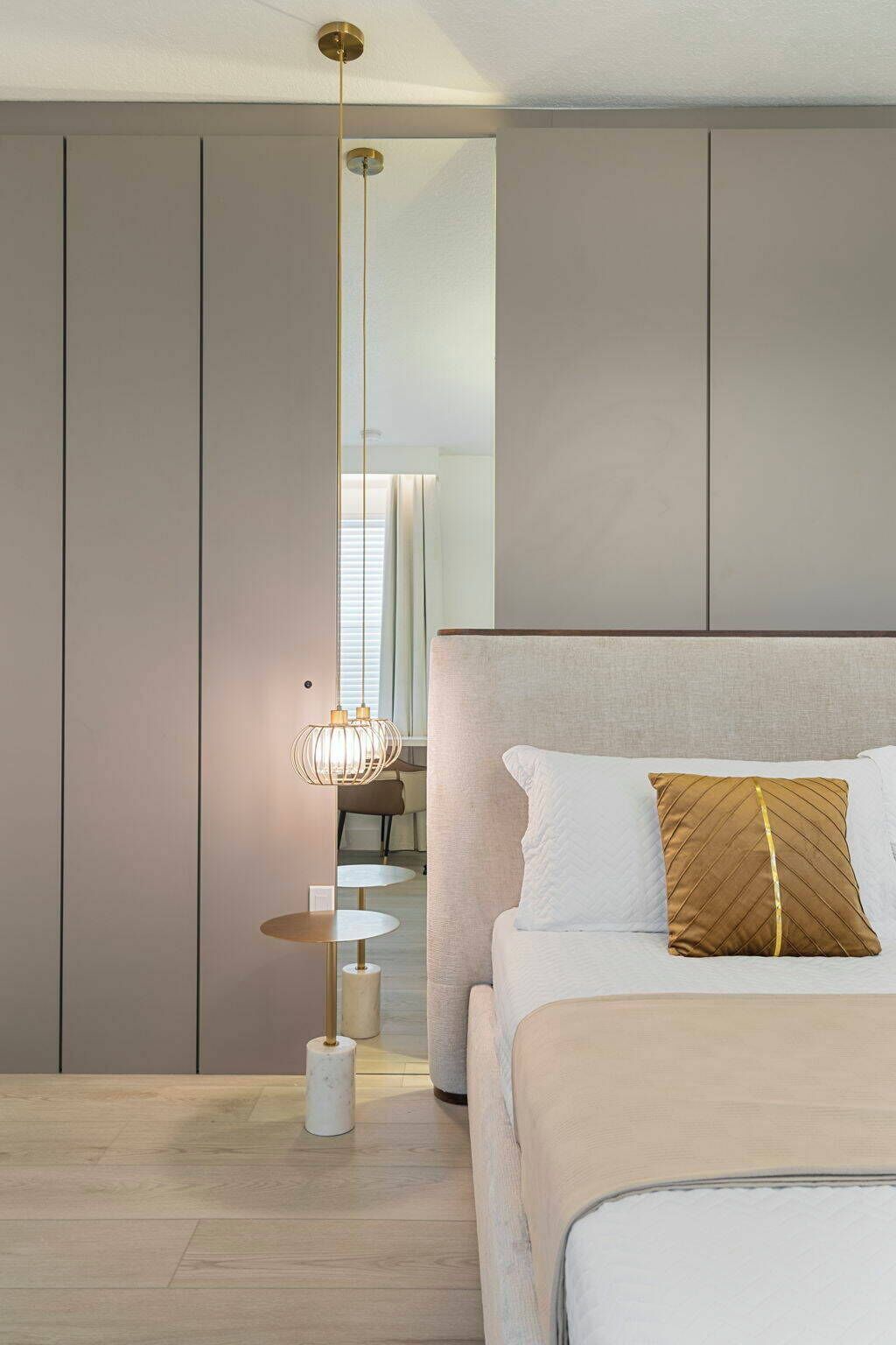 This cozy bedroom features soft beige tones and a plush bed adorned with a decorative pillow, creating a soothing atmosphere. A stylish pendant light and sleek cabinetry enhance the modern decor while offering functional elegance.