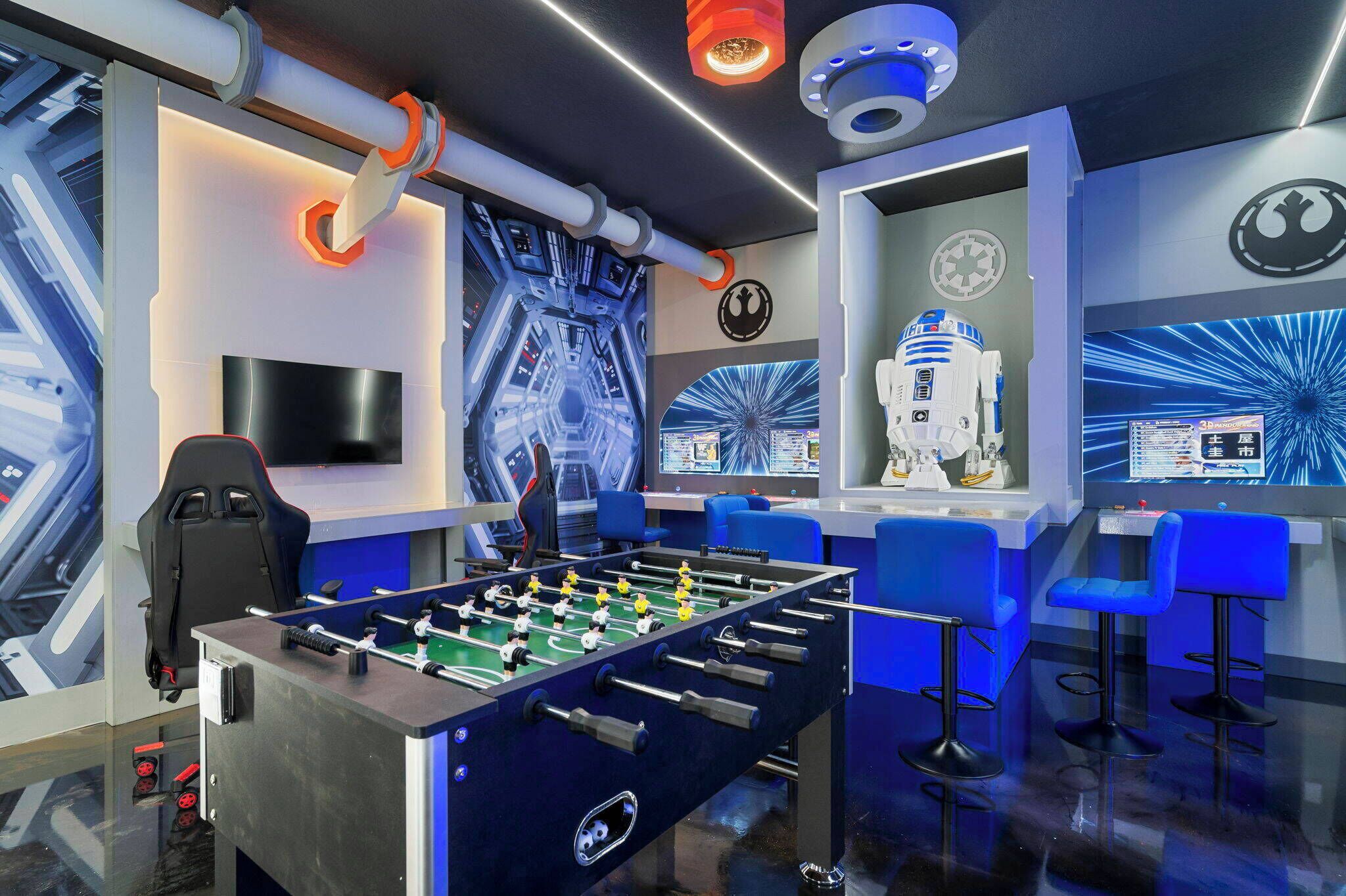 A room with a foosball table, a gaming chair, and Star Wars-themed decor including a R2-D2 figure and a Millennium Falcon model.