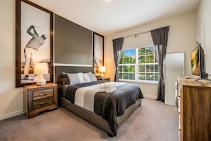 Un dormitorio con cama, mesitas de noche, televisor y ventana con cortinas.