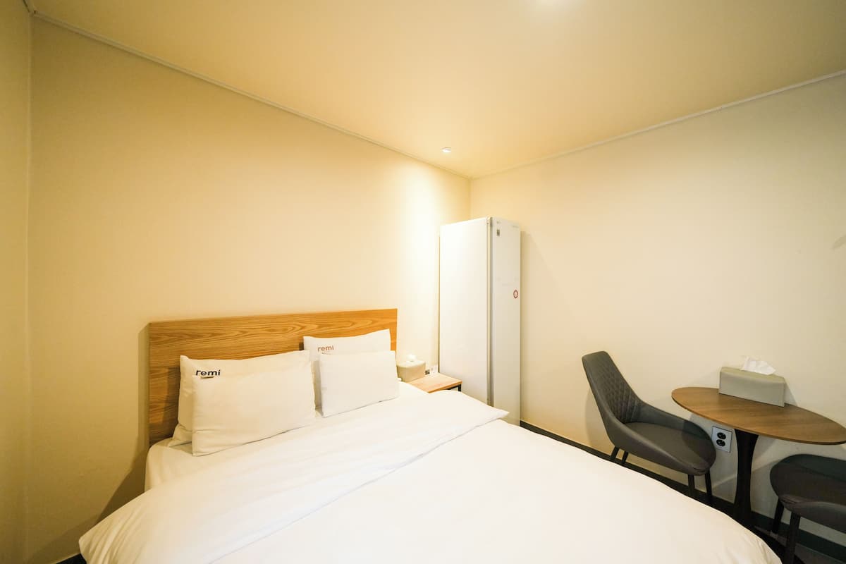 A hotel room with a bed, a wooden headboard, a nightstand, a desk with a chair, and a mirror.