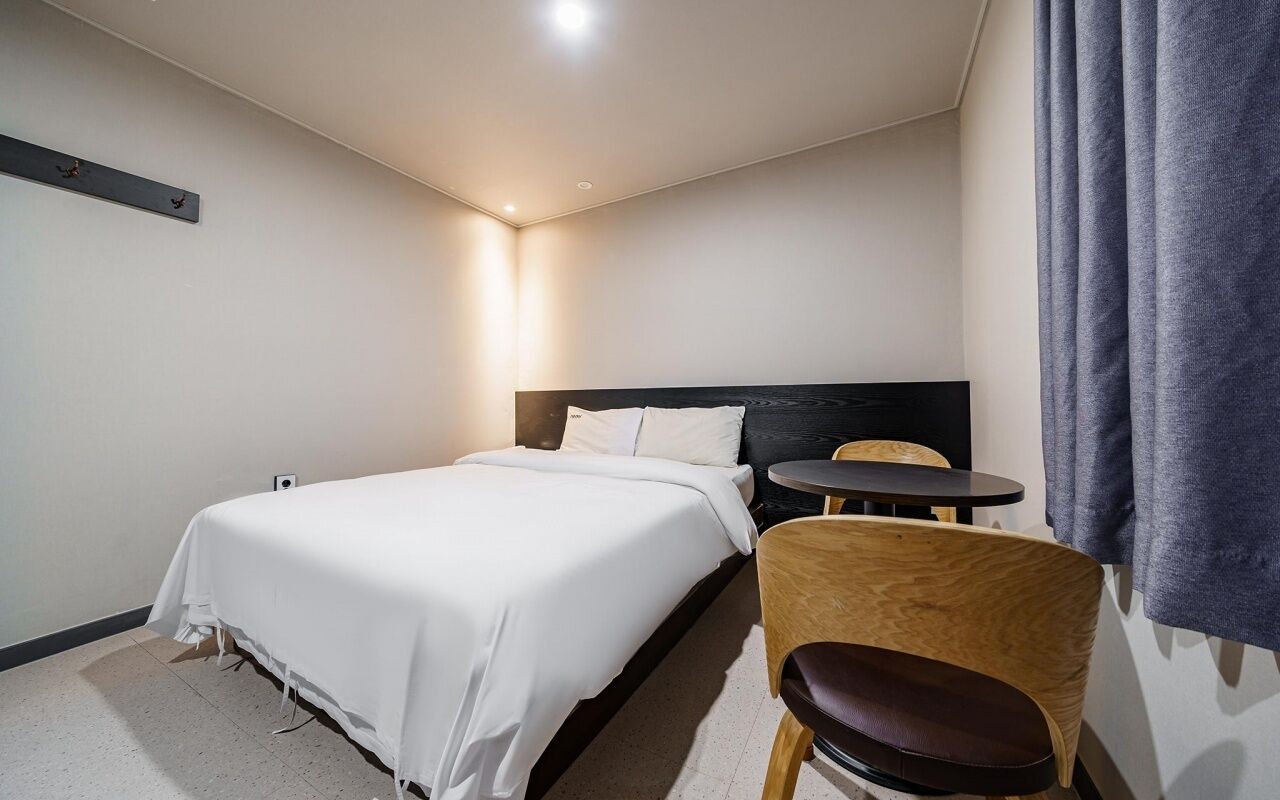 Habitación de hotel con cama, una mesita redonda, una silla y una ventana con cortinas.