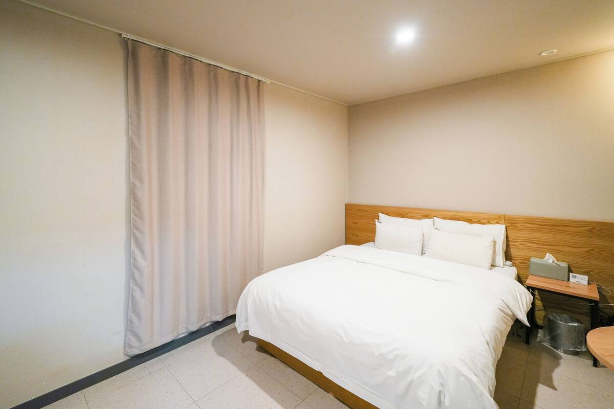 A hotel room with a large bed, a wooden headboard, a nightstand with a tissue box, and a trash bin.