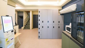 A hotel lobby with a reception desk, a staircase, lockers, and a refrigerator with bottled water. - Hotel remi (Seoul)