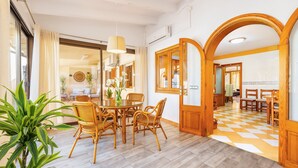 A dining area with a round table and wicker chairs, a large potted plant, and a checkered floor pattern.