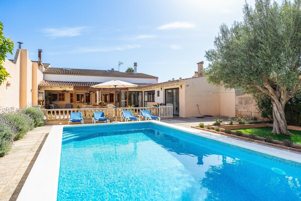 Ein Swimmingpool mit blauem Wasser, umgeben von Liegestühlen und einer überdachten Terrasse.