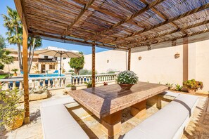 Eine Terrasse im Freien mit einem gefliesten Tisch, weiß gepolsterten Sitzmöglichkeiten, einem Pool und einem überdachten Bereich mit Holzboden.