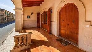A building entrance with a tiled porch, wooden doors, and a stone wall.