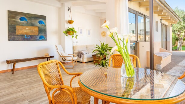 A modern living room with a glass table, wicker chairs, a sofa, and a large window.