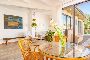 Una sala de estar moderna con una mesa de vidrio, sillas de mimbre, un sofá y un ventanal grande.