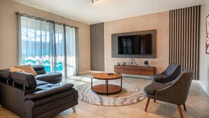 Un salon moderne avec un canapé, un fauteuil, une table basse ronde, un téléviseur et une vue sur l’extérieur.