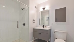 Moderni kylpyhuone, jossa on lasiseinäinen suihkukaappi, valkoinen pesuallas peilillä sekä wc-istuin.