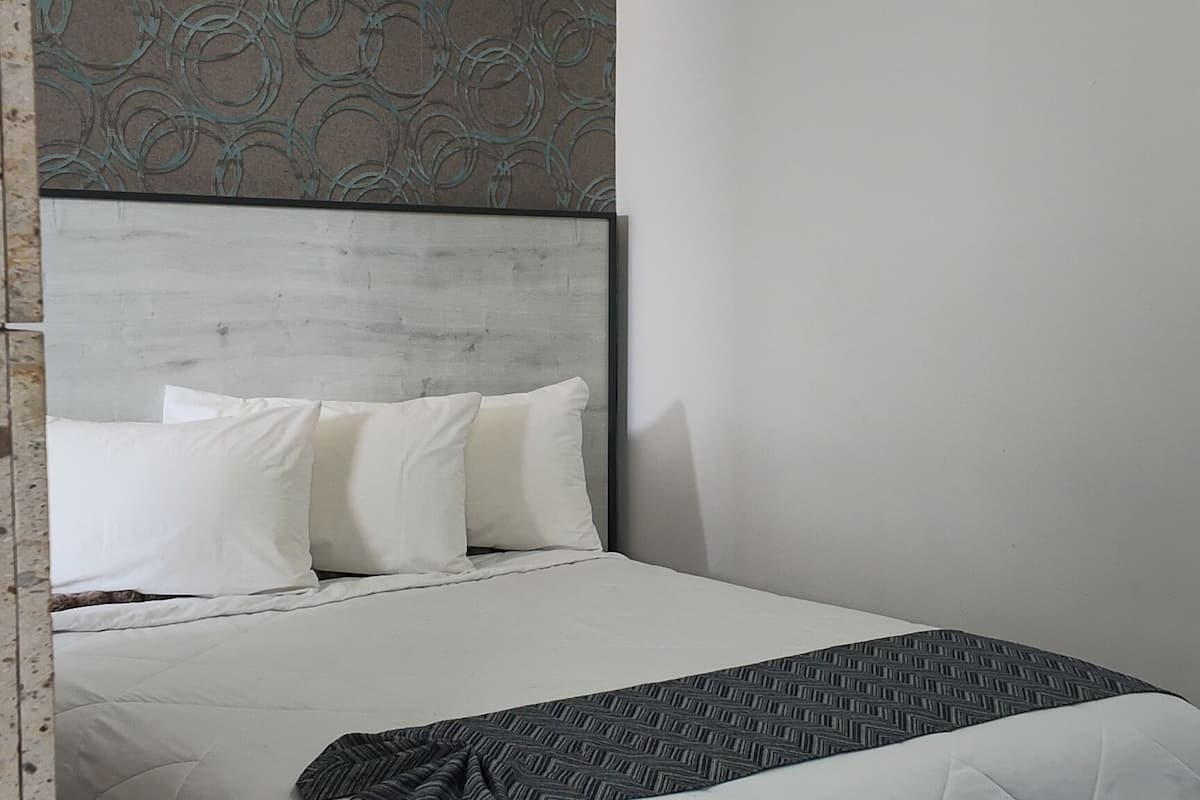 A modern bedroom with a bed, pillows, a blanket, and a headboard with a patterned design.