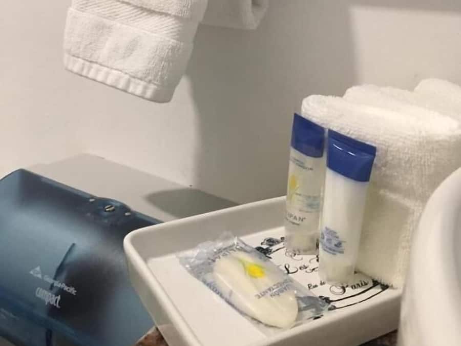 A bathroom with a white towel hanging on a rack, a white sink, and toiletries on a tray.
