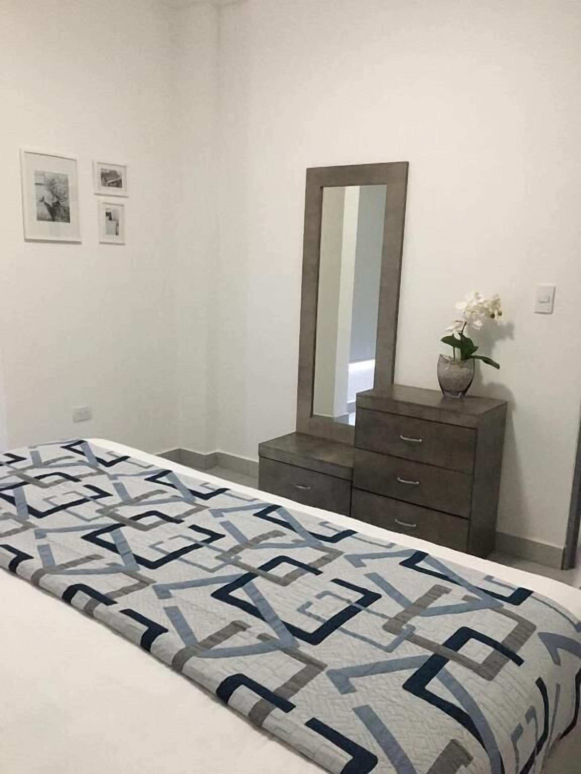Un dormitorio con cama, cómoda, espejo y dos cuadros en la pared.