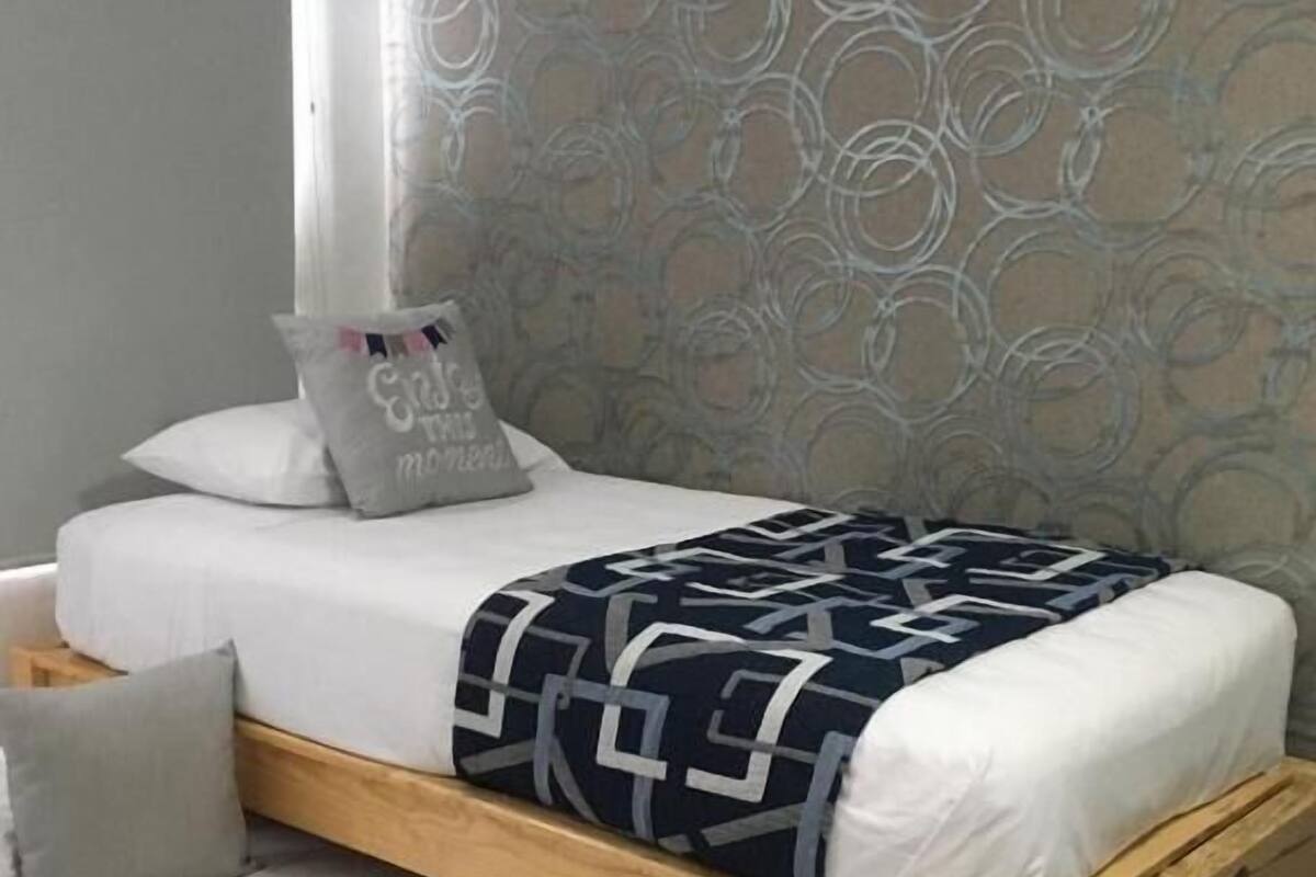 A single bed with a wooden frame, white bedding, and a patterned throw blanket.