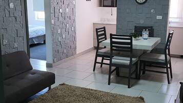 Ein modernes Wohnzimmer mit einer Couch, einem Essbereich mit Stühlen und einem Tisch, einer Küche mit einer Mikrowelle und einer Uhr an der Wand.