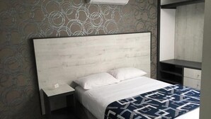 Ein Hotelzimmer mit Bett, Nachttisch, Kommode und Klimaanlage.