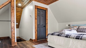 A bedroom with a sloped ceiling, wooden flooring, a bed with a patterned bedspread, and a door.