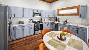 A modern kitchen with grey cabinets, a wooden ceiling, and a dining area with a table set for two.