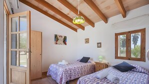 A room with two beds, a wooden door, a ceiling fan, and a window with a view of palm trees. - Villa 'Las Palmeras' with Mountain View, Wi-Fi and Air Conditioning (Illes Balears)