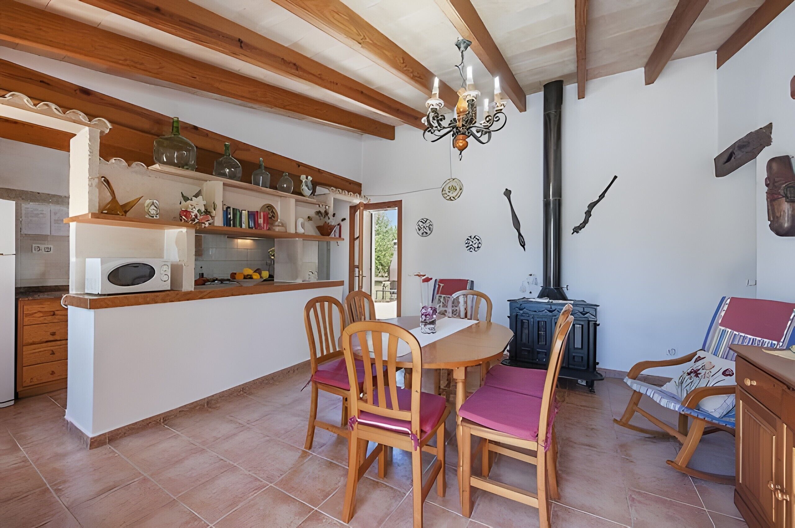 A dining area with wooden chairs and a table, a kitchen with shelves, and a chimney.