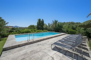 Ein rechteckiger Swimmingpool mit Sprungbrett, umgeben von einer Steindeck und einer Reihe von Liegestühlen.