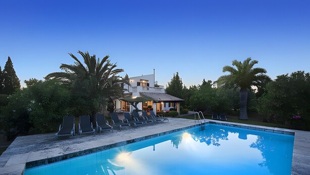 En pool med solstolar, ett hus med en balkong och palmer.