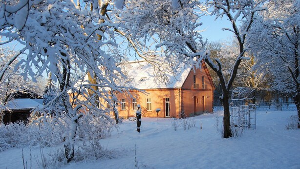 Een gebouw met een rode gevel, bedekt met sneeuw, omringd door bomen en een besneeuwde tuin.