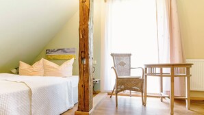 Een slaapkamer met een bed, een houten zuil, een rieten stoel en een tafel.