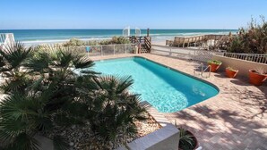 Ein Poolbereich mit Blick auf das Meer, umgeben von Palmen und Topfpflanzen.