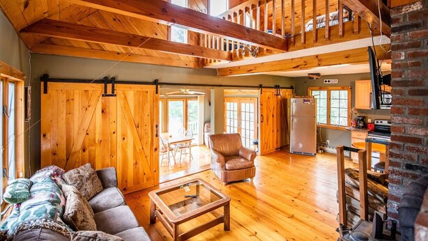 Ein geräumiges Wohnzimmer mit hohen Decken, Holzböden, einem großen Sofa, einem Couchtisch und einer Küchenzeile mit Kühlschrank und Herd.