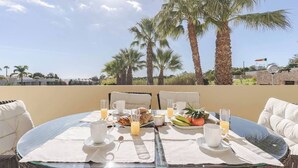 A breakfast table with a view of palm trees and a clear sky. - Palm Breeze Retreat in Albufeira w/ Pool & Balcony (Albufeira)
