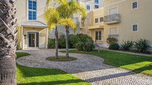 A multi-story building with a paved courtyard, palm trees, and a cobblestone pathway. - Palm Breeze Retreat in Albufeira w/ Pool & Balcony (Albufeira)
