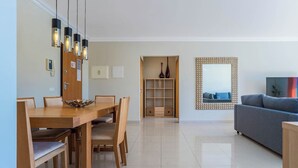 A modern living room with a sofa, a dining area with a wooden table and chairs, and a decorative mirror on the wall. - Palm Breeze Retreat in Albufeira w/ Pool & Balcony (Albufeira)