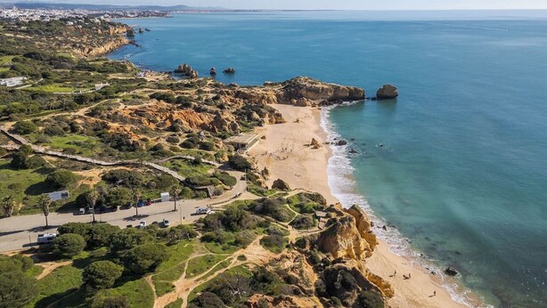 An aerial view of a coastal area with a beach, rocky terrain, and a clear blue sea. - Palm Breeze Retreat in Albufeira w/ Pool & Balcony (Albufeira)