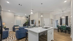 Una cucina moderna con isola centrale, zona pranzo con sedie verdi e un soggiorno con divani blu.