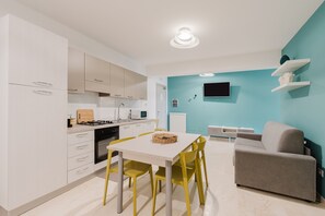 Una cucina moderna con mobili bianchi, un tavolo da pranzo con sedie gialle e un divano grigio in un soggiorno con pareti color verde acqua.