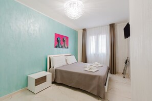A hotel room with a bed, a bedside table, a wall-mounted TV, and a window with curtains. - Azzurra Apartments Trinacria with Sea View, Wi-Fi, and Air Conditioning (Balestrate)