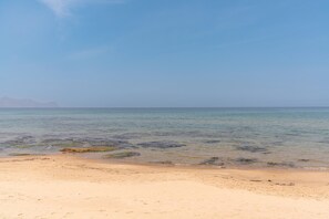 Uma praia com águas cristalinas, montanhas ao longe e uma faixa de areia.