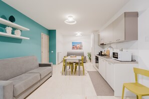 A modern kitchen with white cabinets, a dining table with yellow chairs, and a grey sofa in a bright living area. - Azzurra Apartments Trinacria with Sea View, Wi-Fi, and Air Conditioning (Balestrate)