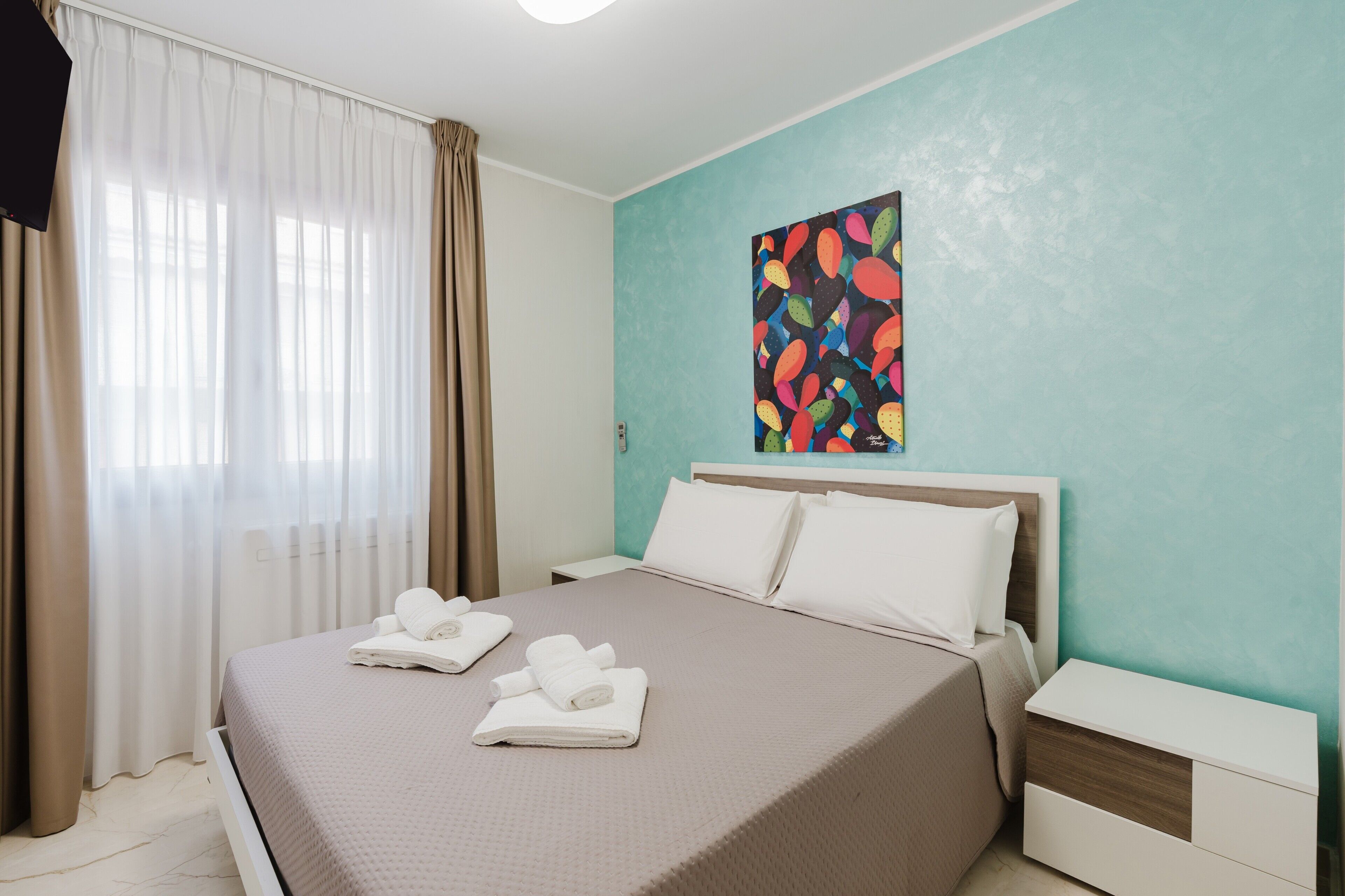 Habitación de hotel con cama, mesita de noche, un cuadro en la pared y una ventana con cortinas.