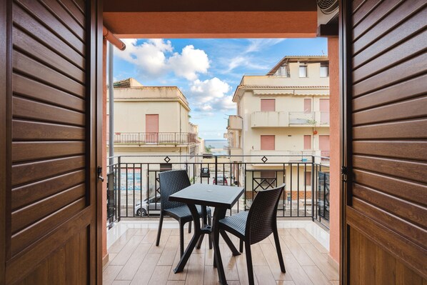 A balcony with a table and chairs, overlooking a residential area with buildings and a clear sky. - Azzurra Apartments Trinacria with Sea View, Wi-Fi, and Air Conditioning (Balestrate)