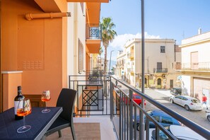 A balcony with a table and chairs, a bottle of wine, and a glass of red wine. - Azzurra Apartments Trinacria with Sea View, Wi-Fi, and Air Conditioning (Balestrate)