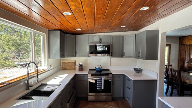 Una cucina moderna con mobili grigi, elettrodomestici in acciaio inossidabile e soffitto in legno.
