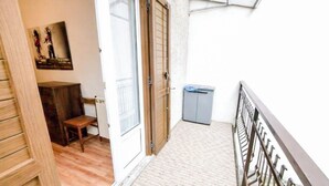 En smal balkon med gelænder i metal, en lille skraldespand og en dør ind til et rum med en træbænk og en radiator.