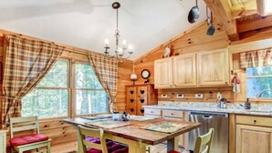 L’intérieur d’un chalet en bois comprend une table à manger, des chaises, un lustre et un coin cuisine.