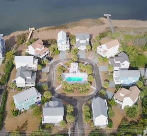 An aerial view of a residential area with houses, a central swimming pool, and a road. - Charming 3-BR house, ocean views, community saltwater pool and fishing dock.  (North Topsail Beach)