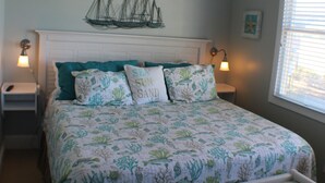 A bedroom with a bed, a nightstand, a bedside table, a ceiling fan, and a window with blinds. - Charming 3-BR house, ocean views, community saltwater pool and fishing dock.  (North Topsail Beach)