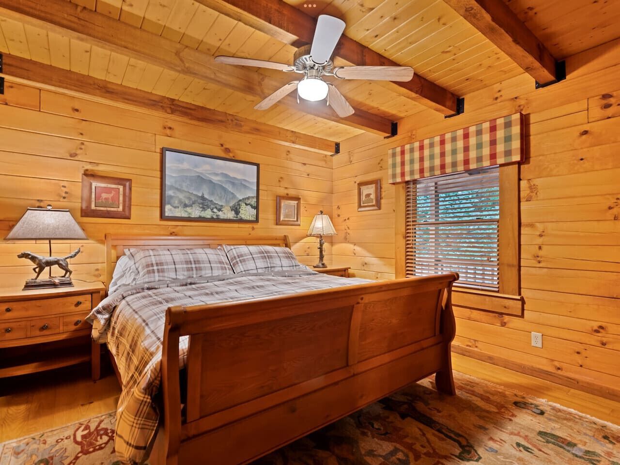 A wooden cabin bedroom with a bed, nightstands, a ceiling fan, and a window with blinds.